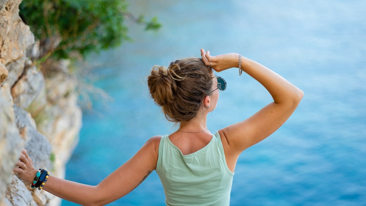 Woman looking out at the blue ocean from a cliff.