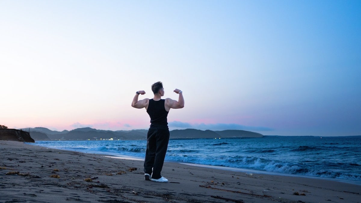 A person flexing muscles on a beach at sunset.